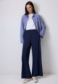 Pantalones de pierna ancha en navy con una cintura elástica, combinados con una camiseta blanca y una camisa de botones a rayas azules. Zapatillas completan el look.