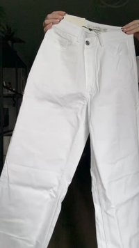 Jeans de mezclilla blanca con un diseño de pierna recta, que cuentan con un cierre frontal de botón, ansilas para cinturón y bolsillos traseros. Textura suave y acabado liso.