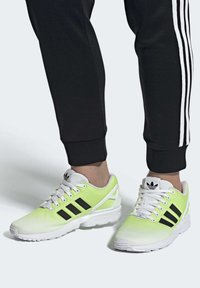 Light green and white athletic shoes with mesh texture, black stripes, and prominent branding. Paired with black athletic pants featuring white stripes.