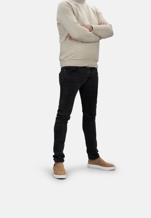 Suéter de punto beige con textura acanalada, jeans negros ajustados y zapatos de lona color beige. Atuendo casual con colores y texturas contrastantes.