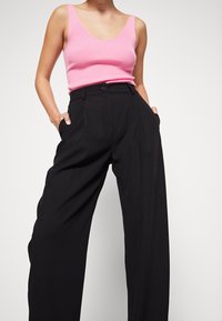 Débardeur rose côtelé avec un large décolleté, associé à un pantalon noir taille haute avec une fermeture à boutons et des poches latérales.