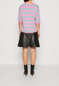 Pull rayé multicolore en vert menthe et rose, associé à une jupe en cuir noire et des bottines noires à bout pointu.