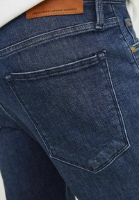 Jeans de mezclilla oscura con una textura suave, que cuentan con un bolsillo trasero, etiqueta de cuero y costuras en contraste.