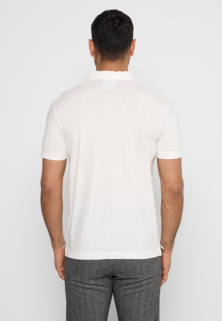 Weißes Kurzarm-Polohemd mit klassischem Kragen, leichtem Stoff und subtiler Textur. Sichtbares Etikett auf der Rückseite.