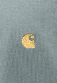 Kortærmet, lysegrøn bomulds skjorte med et lille, broderet gult logo i form af en stiliseret bølge. Glat tekstur.