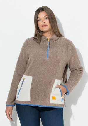 Veste en polaire brun avec un col montant, des zips bleus et des poches plaquées blanches. Présente des accessoires orange et une surface texturée.