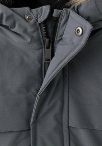 Chaqueta gris, impermeable, con cremallera frontal y cierres a presión, que cuenta con una capucha texturizada y dos bolsillos frontales.