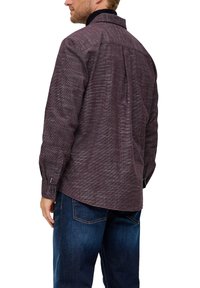 Langärmliges weinrotfarbenes Hemd mit strukturiertem Muster, zwei-Knopf-Manschetten und einem normalen Kragen, kombiniert mit dunkelblauen Jeans.