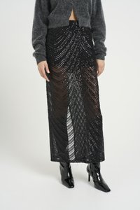 Black sequin skirt with a sheer overlay, featuring wavy patterns. Paired with fitted black glossy heeled boots.