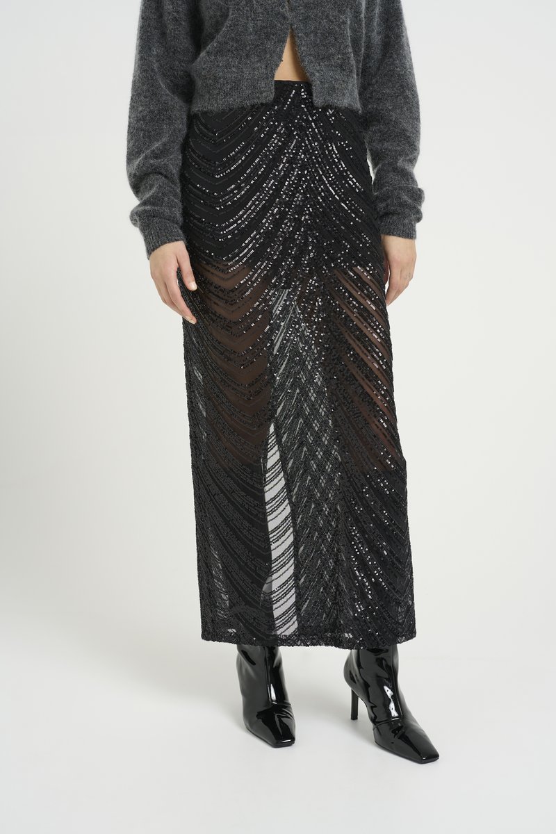 Black sequin skirt with a sheer overlay, featuring wavy patterns. Paired with fitted black glossy heeled boots.