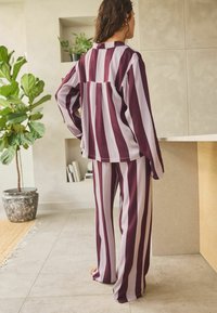 Gestreiftes Loungewear-Set in Weinrot und Hellgrau, mit lockerer Passform, langen Ärmeln und weit geschnittenen Hosen. Hergestellt aus weichem Stoff.