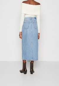 Gonna midi in denim di colore azzurro chiaro, con taglio dritto, due tasche posteriori, abbinata a stivali con tacco neri alla caviglia e a un top bianco a costine off-shoulder.