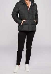 Czarna pikowana kurtka puchowa z kapturem, zapinana na zamek, z dwoma kieszeniami i pikowanym wzorem. W komplecie czarne spodnie i białe buty.