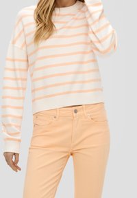 Leichtes, cremefarbenes Sweatshirt mit sanften, pfirsichfarbenen horizontalen Streifen; kombiniert mit pfirsichfarbenen, schmal geschnittenen Jeans. Kurz geschnittenes Design, gerippte Bündchen.