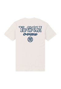 Bílý bavlněný tričko s grafickým designem na zadní straně, na kterém je námořnickomodrý text "Yu-Gi-Oh!" a další japonské znaky.