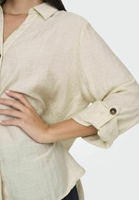 Lichtbeige knoopshirt van een textuurstof, met een kraag en omgerolde mouwen met een knoopdetail. Vlotte, casual uitstraling.
