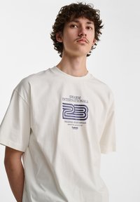 Witte katoenen t-shirt met een grafische print in blauw en zwart, ronde halslijn en korte mouwen.