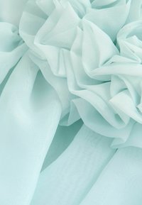 Heledsinine õhuline kangas pehme ja voogava tekstuuriga. Volangide kihid loovad sügavust ja liikumist, tuues esile õrnade ja õhuliste vormide disaini.