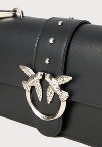 Zwarte leren handtas met een ronde zilveren hardware detail met twee vogelontwerpen. Inclusief zilveren studs op de schouderband.