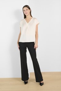 Light beige short-sleeve blouse with a V-neck and pleat detail, paired with black tailored pants; model wearing pointed black heels.