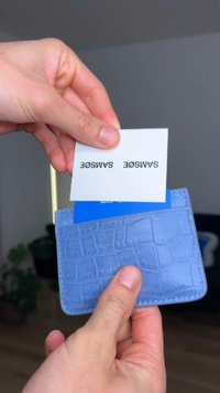 Porte-cartes bleu clair avec un motif texturé semblable à du crocodile, tenu en main avec une carte blanche partiellement insérée.