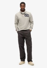 Grijs fleece sweatshirt met knoopsluiting bij de kraag en een marineblauw logo; gecombineerd met donkere cargobroeken met zijzakken en een relaxed fit.