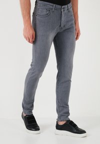 Vaqueros de mezclilla gris con corte ajustado, bolsillos frontales planos y costuras cosidas. Combinados con zapatillas negras con diseño de tiras.