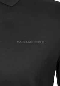 Czarna koszulka polo z klasycznym kołnierzykiem, wykonana z gładkiej tkaniny. Z przodu znajduje się wyraźne, wytłoczone logo "KARL LAGERFELD".