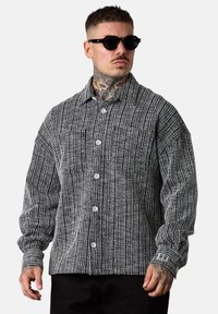 Gestreiftes schwarz-weißes Hemd mit Knopfleiste, verbreitetem Kragen, langen Ärmeln und einer Brusttasche, aus strukturiertem Stoff mit Knöpfen.