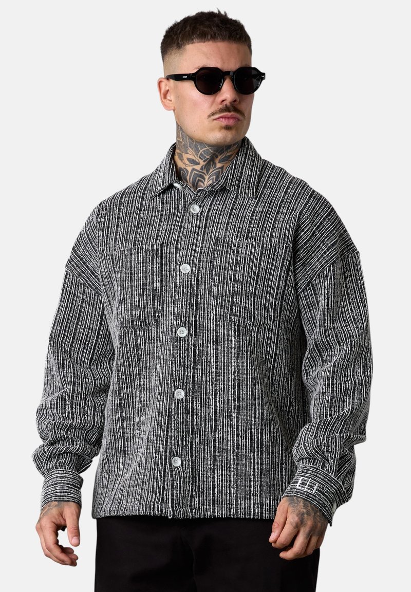 Gestreiftes schwarz-weißes Hemd mit Knopfleiste, verbreitetem Kragen, langen Ärmeln und einer Brusttasche, aus strukturiertem Stoff mit Knöpfen.