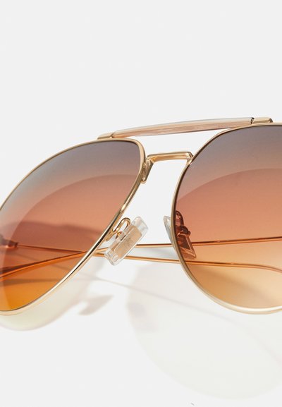 Ochelari de soare aviator din metal aurit, cu lentile graduale maro și un tampon nazal transparent. Acestia au un pod dublu și un design subțire al bratelor.