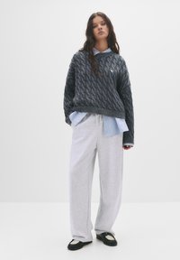 Grå kabelstrikket sweater med ribbet kant, lagd over en lyseblå stribet skjorte, parret med grå sweatpants og sorte sko.