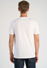 Vit bomullströja med korta ärmar och rund halsringning, med en enkel design och rak nederkant, bärs med mörka jeans.