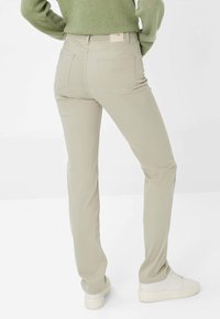 Pantalons droit beige clair en mélange de coton, dotés de poches arrière et d'une étiquette sur la taille. Portés avec des baskets blanches.