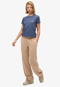 Granatowy bawełniany t-shirt z okrągłym dekoltem i białym napisem, zestawiony z beżowymi szerokimi spodniami i jasnymi sneakersami.