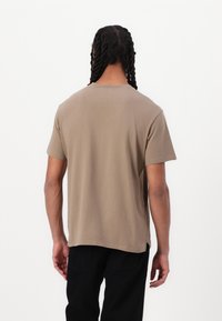 Kortærmet t-shirt med rund hals i lysebrun bomuld, med en afslappet pasform og ren kant, båret med sorte bukser, set fra ryggen.