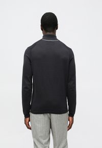 Polo preta de manga comprida com gola alta, apresentando uma faixa branca de destaque ao longo do decote. Material suave e design ajustado.