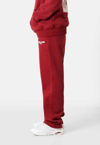 Rote Jogginghosen aus weichem Stoff, mit lockerem Schnitt, Seitentaschen und weißen Logo-Details in der Nähe des Knöchels und des Bunds.