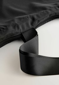 Melna auduma soma ar rāvējslēdzēja aizdari un teksturētu melnu siksnu, ar gludu virsmu un nelielu spīdumu, bez redzamām rakstiem.