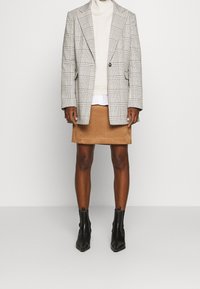 Blazer à carreaux gris clair avec accents noirs, col roulé crème, mini jupe en daim beige, et bottines noires à bouts pointus.