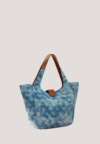 Sac cabas en denim bleu avec un motif monogramme blanc discret, des anses en cuir marron et une fermeture par sangle en cuir marron sur fond uni.