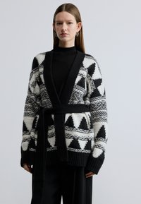 Ανοιχτό μαύρο και άσπρο ζακέτα με γεωμετρικά σχέδια, ριμπ μανσέτες και ζώνη στη μέση, κατασκευασμένη από υφή πλεκτό υλικό.