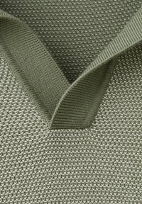 Zbliżenie na zieloną dzianinę o fakturze z nakładającymi się prążkowanymi brzegami tworzącymi kształt litery V.