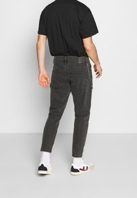 Czarny T-shirt, szare dżinsy o dopasowanym kroju z tylnymi kieszeniami i łańcuszkiem na pętli od paska, zestawione z białymi tenisówkami.