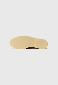 Beige rubber sole with a smooth texture, featuring a slight curve at the heel and an embossed logo detail near the heel.