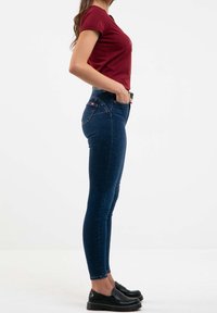 Smala jeans i mörkblå denim med en lätt lyster, kombinerat med en figurnära vinröd t-shirt och svarta slip-on skor.