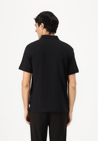 Zwarte polo met een klassieke kraag, korte mouwen en een zachte textuur. Gezien van de achterkant, zonder patronen of accenten zichtbaar.