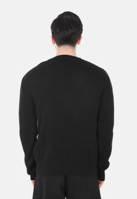 Maglione nero a maglia con un motivo tessuto, scollo rotondo e maniche lunghe, caratterizzato da una vestibilità rilassata e spacchi laterali all'orlo.