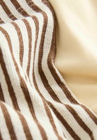 Nahaufnahme eines weichen Stoffs mit strukturierten braunen und cremefarbenen Streifen neben glattem beigem Stoff, der Falten und gewebte Muster zeigt.