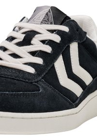 Baskets en daim bleu foncé avec des accents en cuir blanc en forme de chevron et des lacets crème. Semelle en caoutchouc avec motifs texturés, design minimaliste.